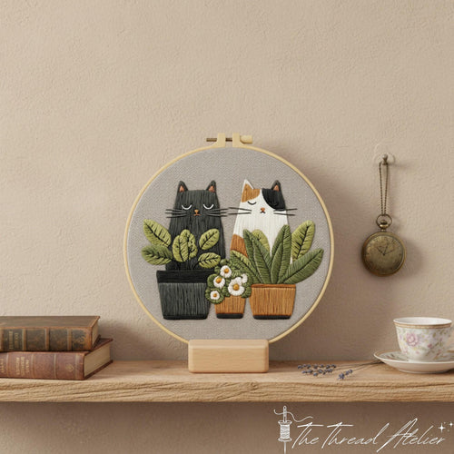 Cats and houseplants hoop art on its stand between old books and a pocket watch