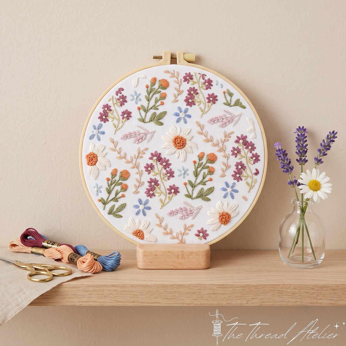 Wildflower daisy hoop art on a wooden stand beside lavender, a white daisy and colorful floss